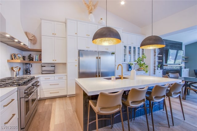 kitchen with sink, wall chimney range hood, vaulted ceiling, white cabinets, and high end appliances