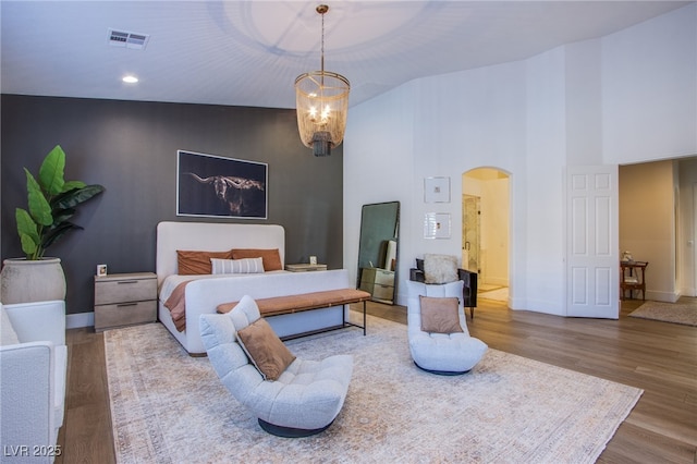 bedroom featuring hardwood / wood-style floors, a towering ceiling, and a notable chandelier