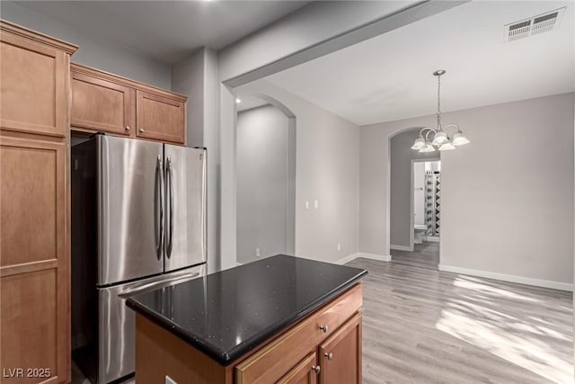 kitchen featuring a center island, a notable chandelier, stainless steel fridge, pendant lighting, and light wood-type flooring