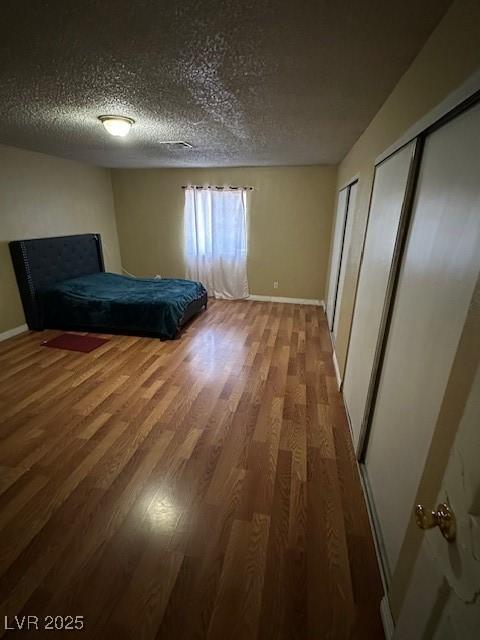 unfurnished bedroom with multiple closets, wood-type flooring, and a textured ceiling