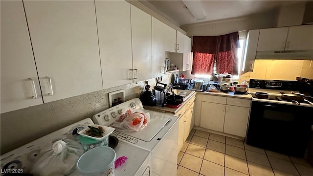 kitchen featuring sink, black electric range, light tile patterned floors, washing machine and dryer, and white cabinets