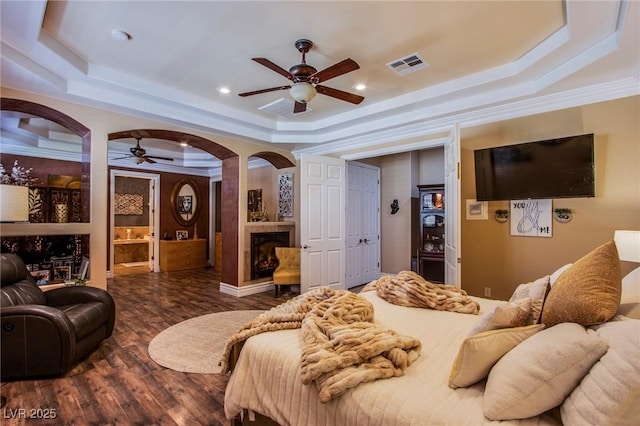 bedroom featuring ornamental molding, ceiling fan, connected bathroom, dark hardwood / wood-style floors, and a tray ceiling