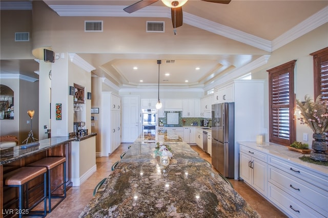 kitchen with white cabinetry, stainless steel appliances, dark stone counters, hanging light fixtures, and a breakfast bar