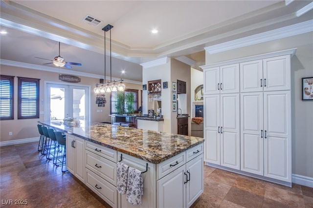 kitchen featuring white cabinets, a center island, ornamental molding, and dark stone counters