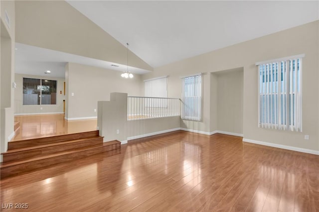 spare room with hardwood / wood-style floors, high vaulted ceiling, and a notable chandelier