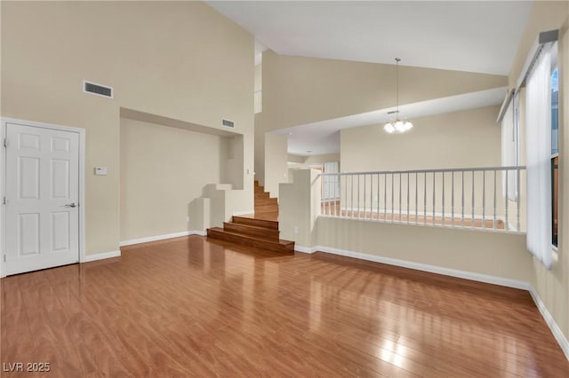 unfurnished living room featuring hardwood / wood-style flooring, high vaulted ceiling, and a chandelier