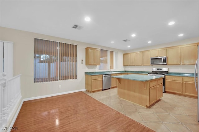 kitchen with appliances with stainless steel finishes, light brown cabinetry, sink, light tile patterned floors, and a center island