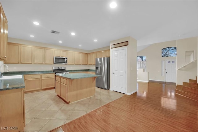 kitchen with light brown cabinets, a center island, sink, light tile patterned floors, and appliances with stainless steel finishes