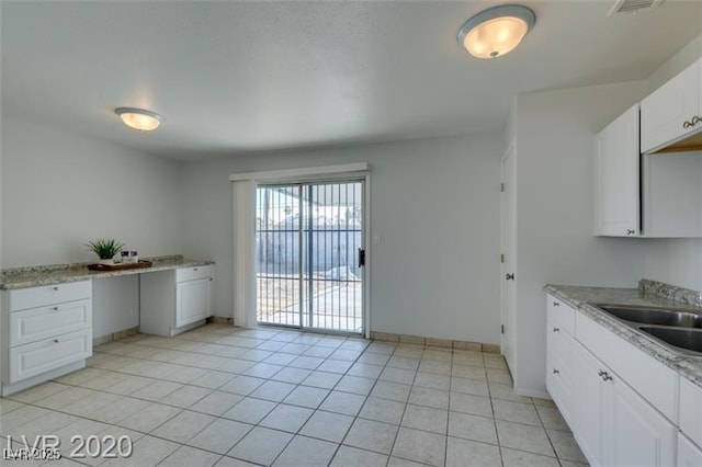 kitchen featuring white cabinets, light tile patterned floors, light stone counters, and sink