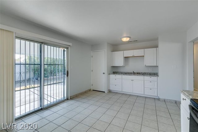 kitchen with white cabinetry, sink, light tile patterned floors, and light stone counters