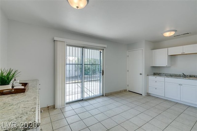 kitchen with white cabinets, light tile patterned flooring, light stone countertops, and sink