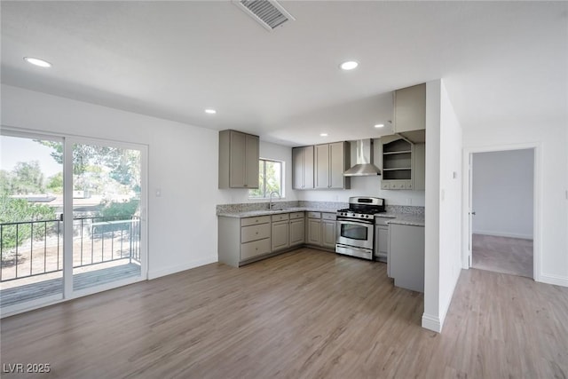 kitchen with sink, wall chimney exhaust hood, gray cabinets, light hardwood / wood-style floors, and gas stove