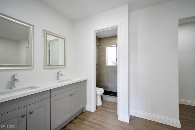 bathroom featuring a tile shower, vanity, wood-type flooring, and toilet