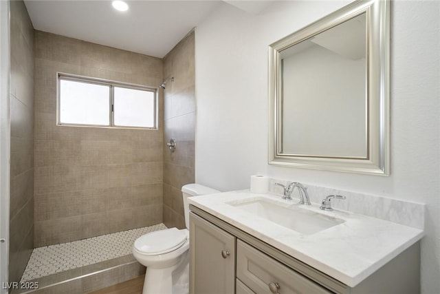 bathroom with a tile shower, vanity, and toilet