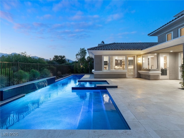 pool at dusk featuring an in ground hot tub, pool water feature, and a patio area