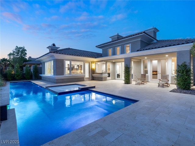 pool at dusk with an in ground hot tub and a patio