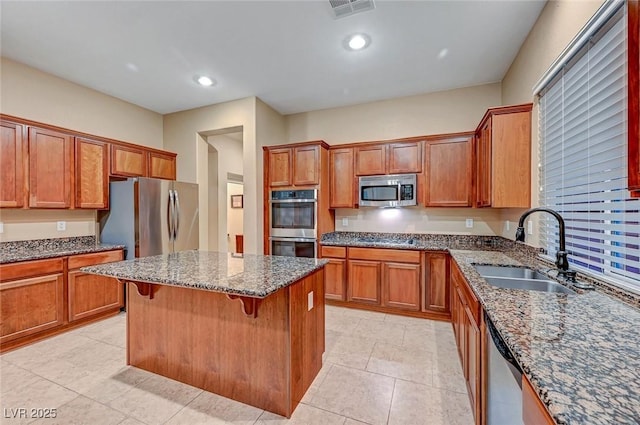 kitchen with sink, dark stone counters, a breakfast bar, a kitchen island, and appliances with stainless steel finishes