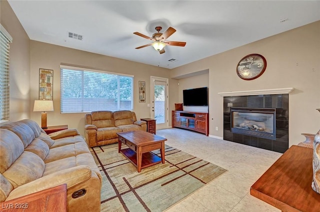 tiled living room with ceiling fan and a tiled fireplace