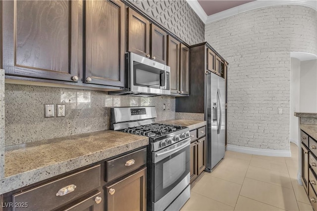 kitchen with dark brown cabinetry, appliances with stainless steel finishes, decorative backsplash, light tile patterned floors, and ornamental molding