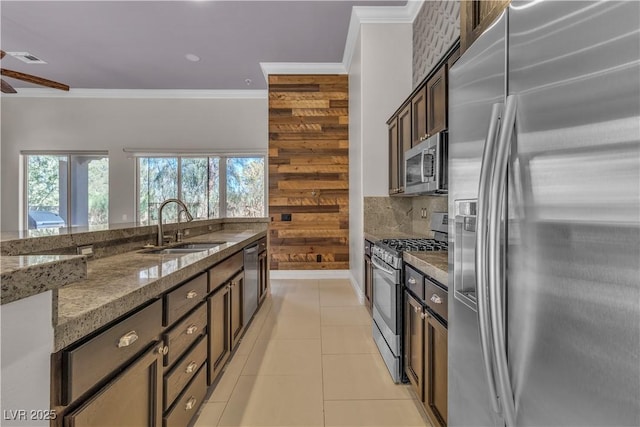 kitchen featuring sink, wooden walls, dark stone countertops, dark brown cabinetry, and stainless steel appliances