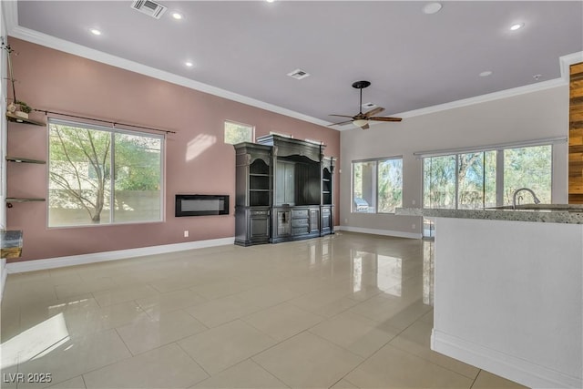 unfurnished living room featuring ceiling fan, light tile patterned floors, ornamental molding, and a wealth of natural light