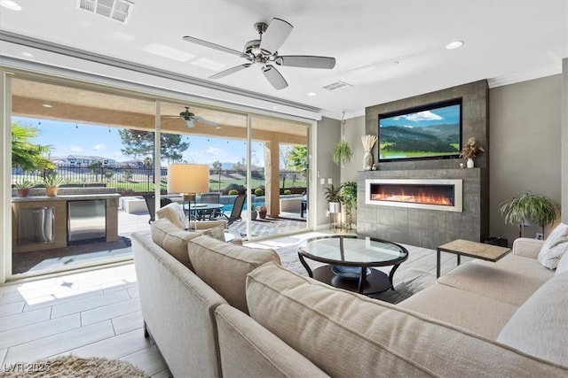 tiled living room featuring crown molding, a large fireplace, and ceiling fan