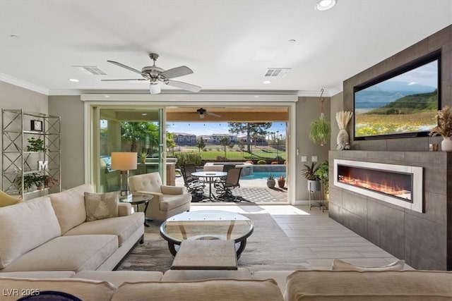 living room featuring a tile fireplace, crown molding, and ceiling fan