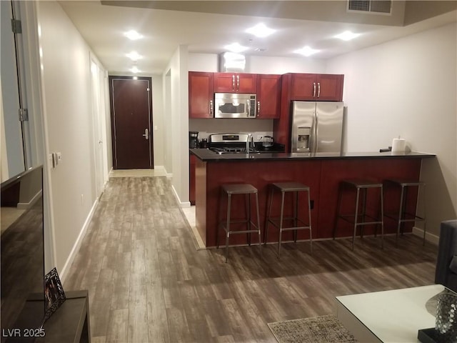 kitchen with kitchen peninsula, a breakfast bar, stainless steel appliances, and wood-type flooring