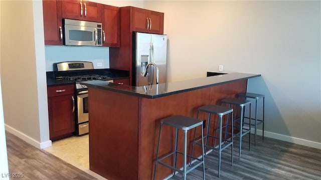 kitchen featuring light hardwood / wood-style floors, kitchen peninsula, stainless steel appliances, and a breakfast bar area