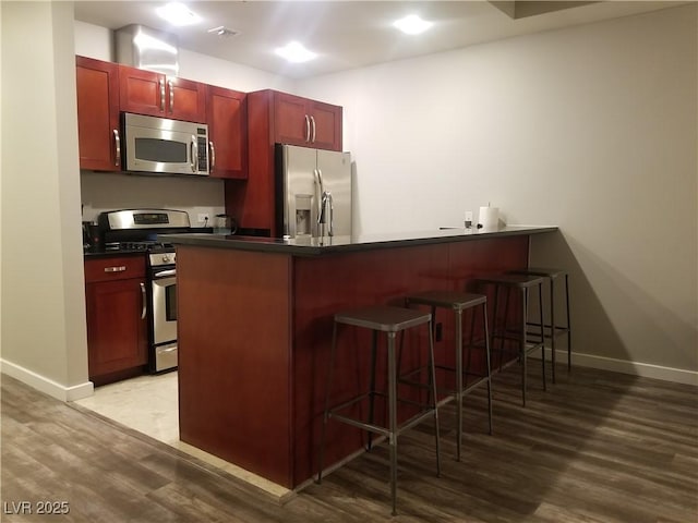 kitchen with kitchen peninsula, a kitchen bar, stainless steel appliances, and light hardwood / wood-style flooring