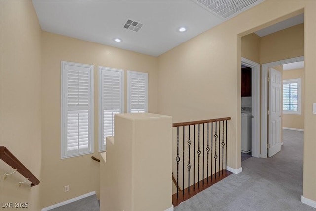 corridor with washer / dryer and light colored carpet