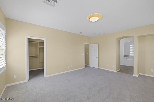 unfurnished bedroom featuring light carpet, ensuite bathroom, a spacious closet, and a closet