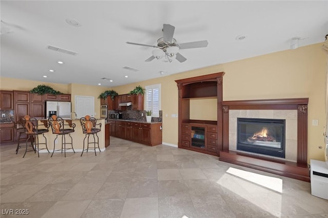 kitchen with a tile fireplace, white fridge with ice dispenser, oven, decorative backsplash, and a breakfast bar