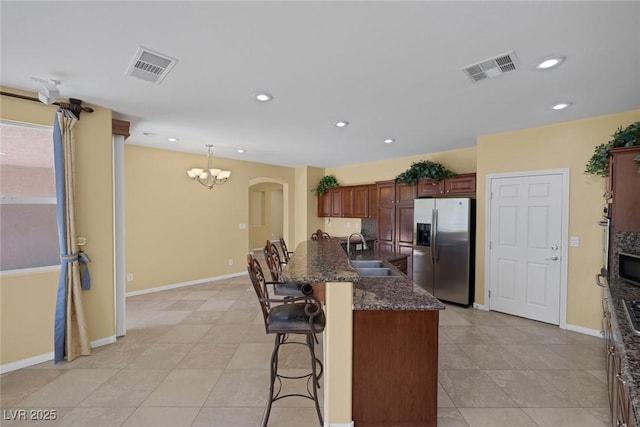 kitchen with a kitchen bar, stainless steel fridge, sink, a notable chandelier, and hanging light fixtures