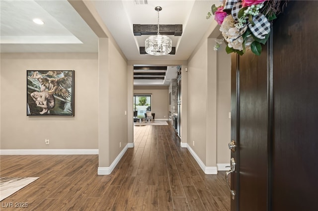 hallway featuring a notable chandelier, dark hardwood / wood-style flooring, and a raised ceiling