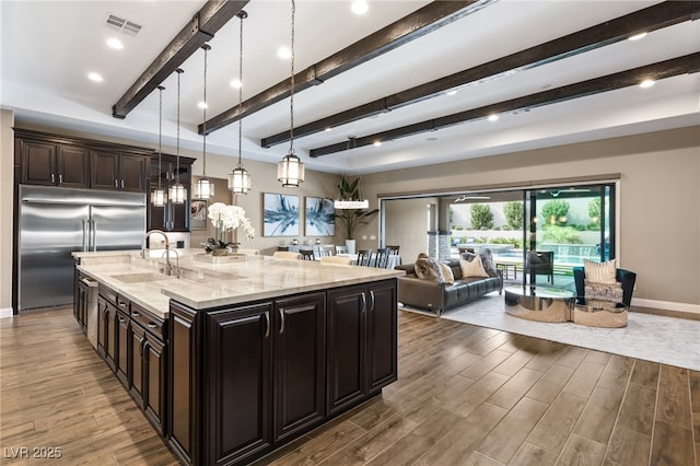 kitchen with stainless steel built in refrigerator, sink, decorative light fixtures, light stone counters, and dark brown cabinets