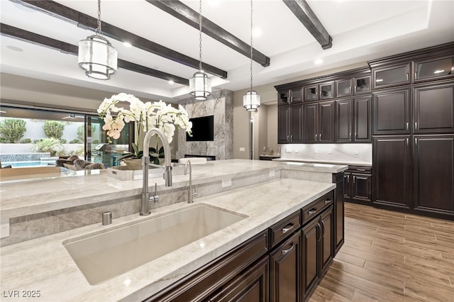 kitchen featuring light stone counters, dark brown cabinets, hanging light fixtures, and sink