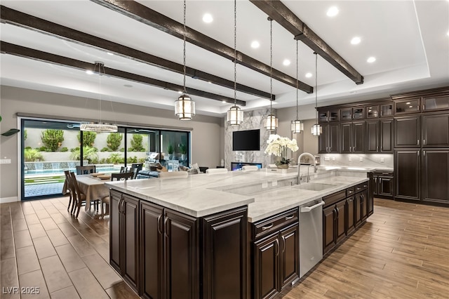 kitchen with pendant lighting, sink, stainless steel dishwasher, light stone countertops, and dark brown cabinetry