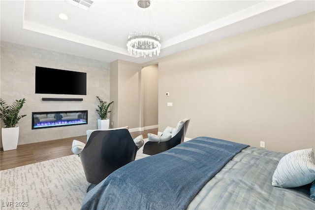 bedroom with an inviting chandelier, hardwood / wood-style flooring, and a raised ceiling