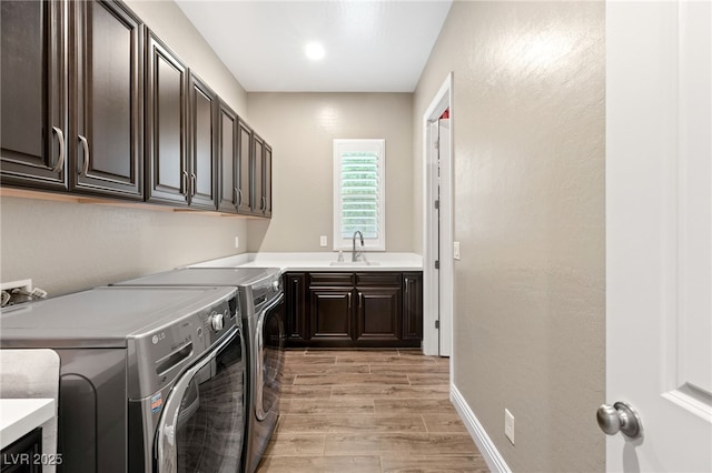 laundry area with washing machine and clothes dryer, sink, cabinets, and light hardwood / wood-style floors