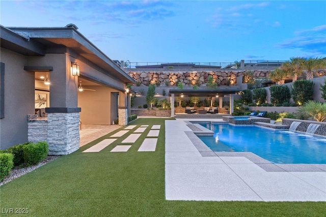 pool at dusk with ceiling fan, an outdoor hangout area, pool water feature, a patio area, and an in ground hot tub