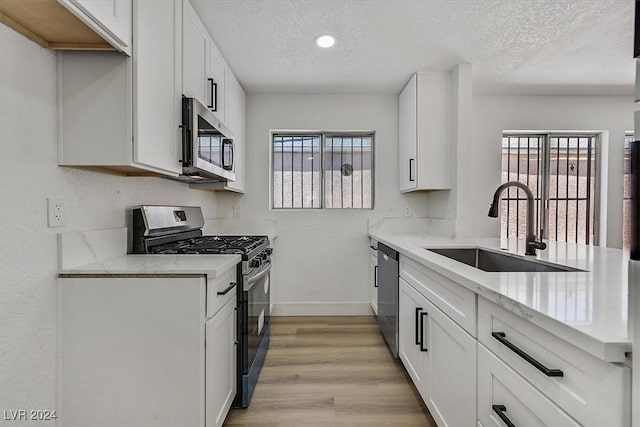 kitchen with white cabinetry, sink, stainless steel appliances, light stone counters, and a textured ceiling