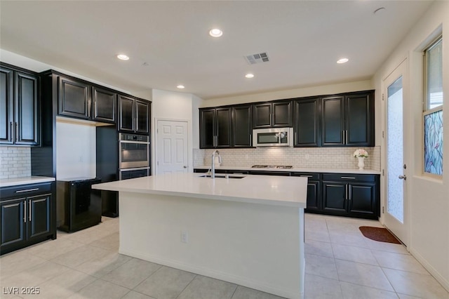 kitchen with appliances with stainless steel finishes, sink, a center island with sink, and light tile patterned floors