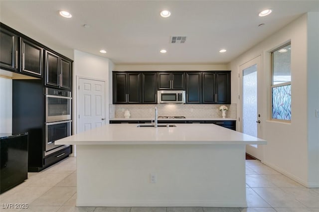 kitchen featuring backsplash, stainless steel appliances, sink, an island with sink, and light tile patterned flooring