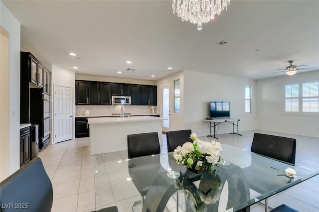 tiled dining room featuring ceiling fan with notable chandelier and sink