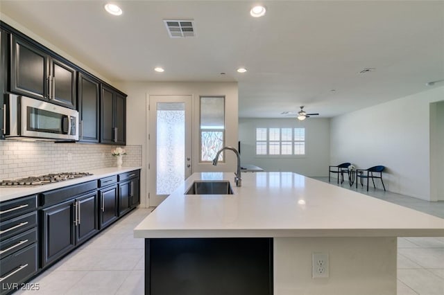 kitchen with backsplash, stainless steel appliances, a kitchen island with sink, and sink