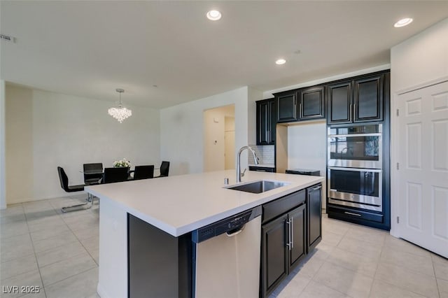 kitchen featuring sink, a kitchen island with sink, stainless steel appliances, tasteful backsplash, and decorative light fixtures