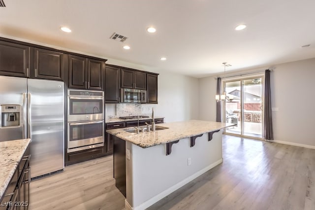 kitchen featuring a kitchen bar, stainless steel appliances, light hardwood / wood-style flooring, and light stone counters