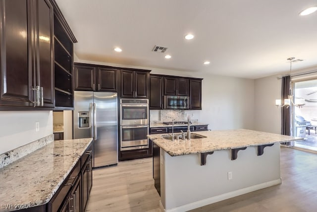 kitchen featuring a kitchen breakfast bar, light wood-type flooring, decorative light fixtures, and appliances with stainless steel finishes