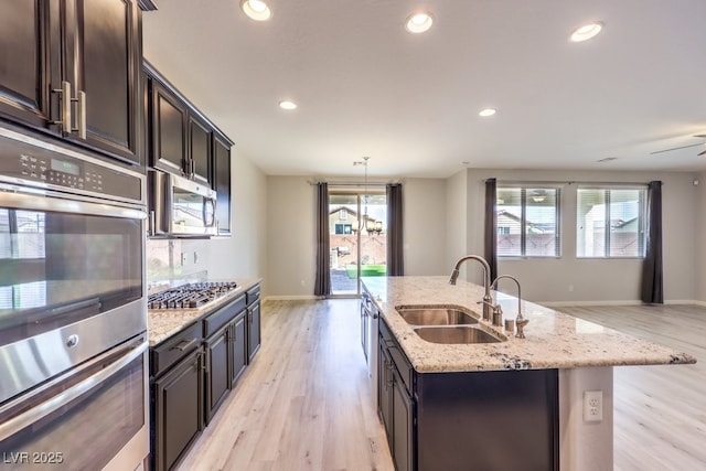 kitchen featuring a kitchen island with sink, sink, light stone countertops, light hardwood / wood-style floors, and stainless steel appliances